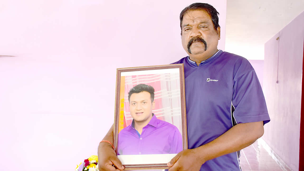 Le caporal Jayraj Boodhoo tenant un portrait de son fils qui était policier.