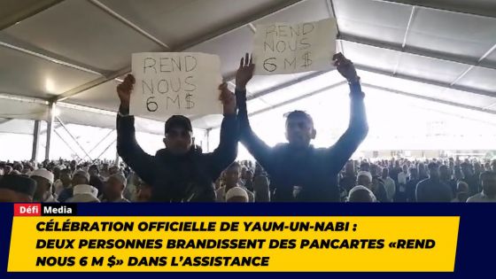 Célébration officielle de Yaum-Un-Nabi : deux personnes brandissent des pancartes «Rend Nous 6 M $» dans l’assistance