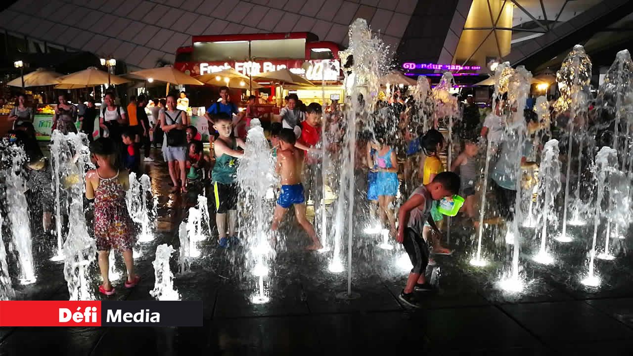 En été, les familles en profitent pour se promener le soir. Ici, dans le centre de la ville, les enfants s’amusent avec les jets d’eau sous la supervision des parents. En début d’été, la température est au alentour de 30 degrés. Shenzhen