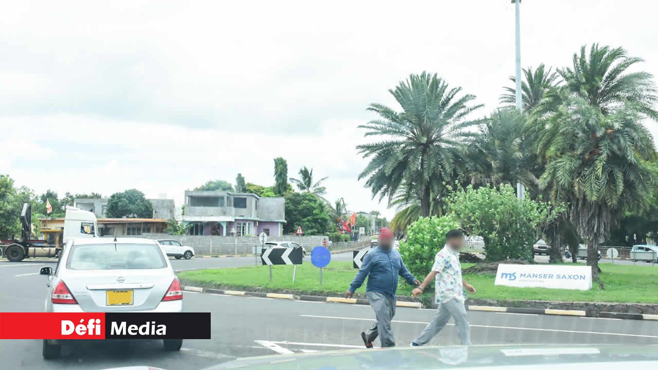Deux personnes se faufilent entre les voitures au rond-point de Riche-Terre.